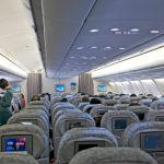 Passageiros ocupam a cabine de um avião enquanto membros da tripulação atendem os viajantes.