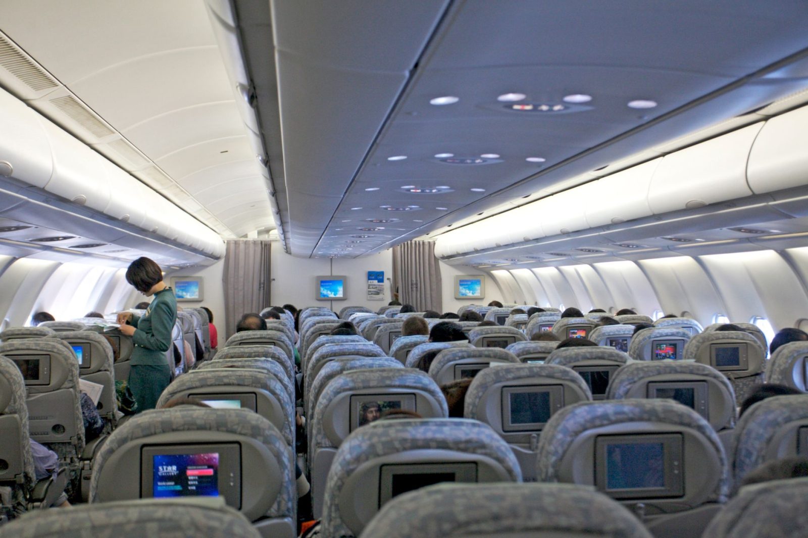 Passageiros ocupam a cabine de um avião enquanto membros da tripulação atendem os viajantes.
