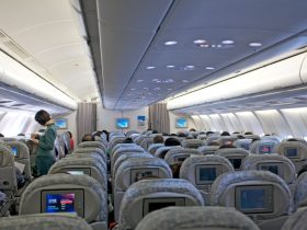 Passageiros ocupam a cabine de um avião enquanto membros da tripulação atendem os viajantes.