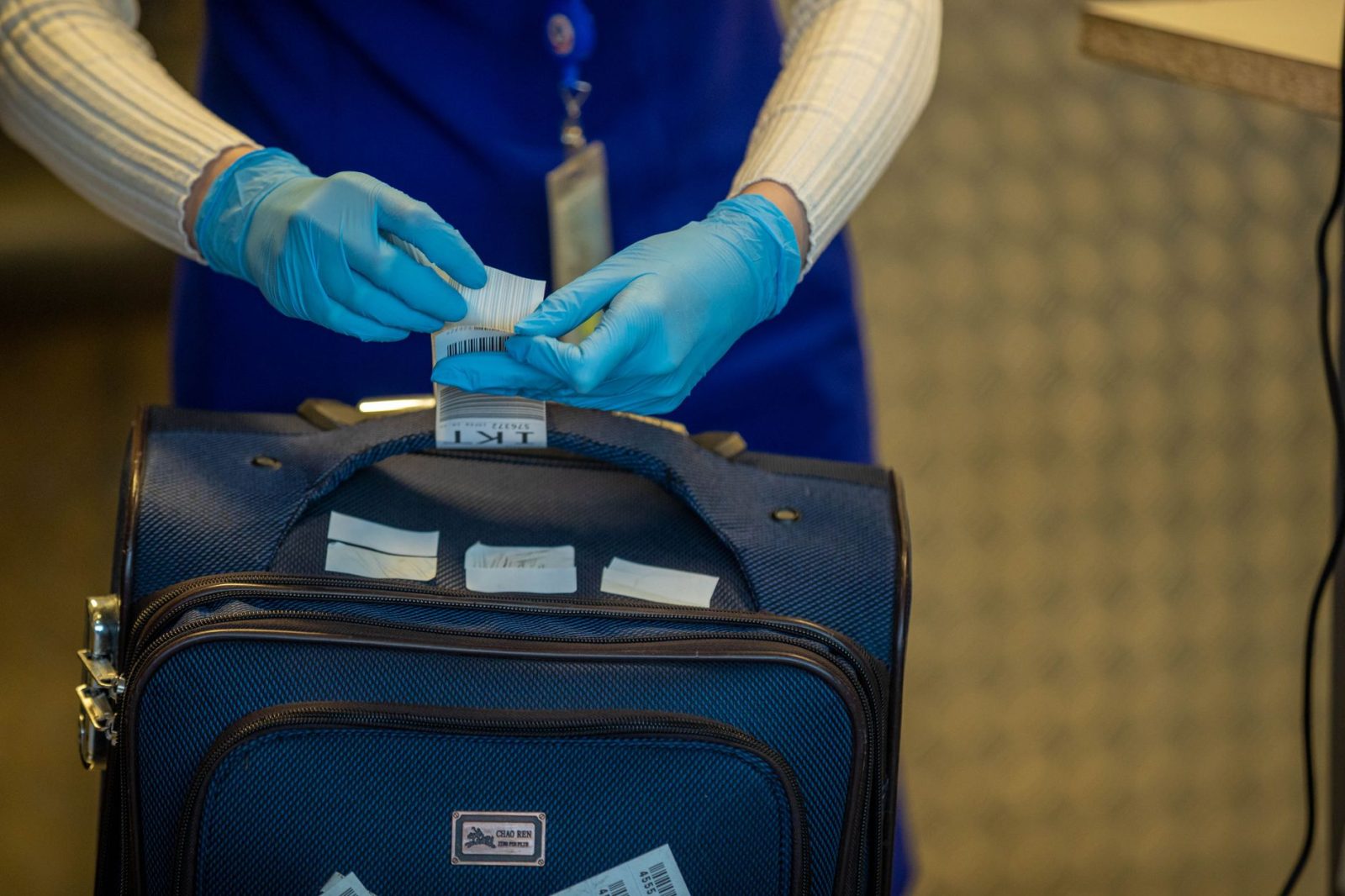 Mãos protegidas por luvas inspecionam etiquetas de bagagem durante procedimento de segurança em aeroporto.