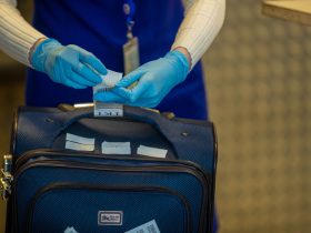 Mãos protegidas por luvas inspecionam etiquetas de bagagem durante procedimento de segurança em aeroporto.
