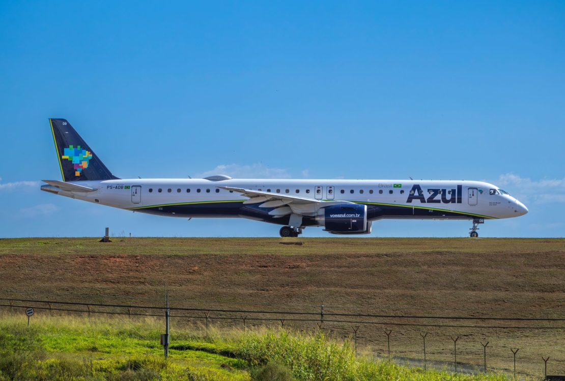 Jato da Embraer da Azul preparado para decolar em um aeroporto, sob céu ensolarado.