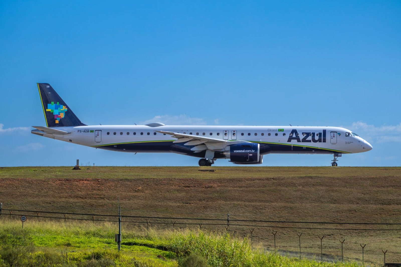 Jato da Embraer da Azul preparado para decolar em um aeroporto, sob céu ensolarado.