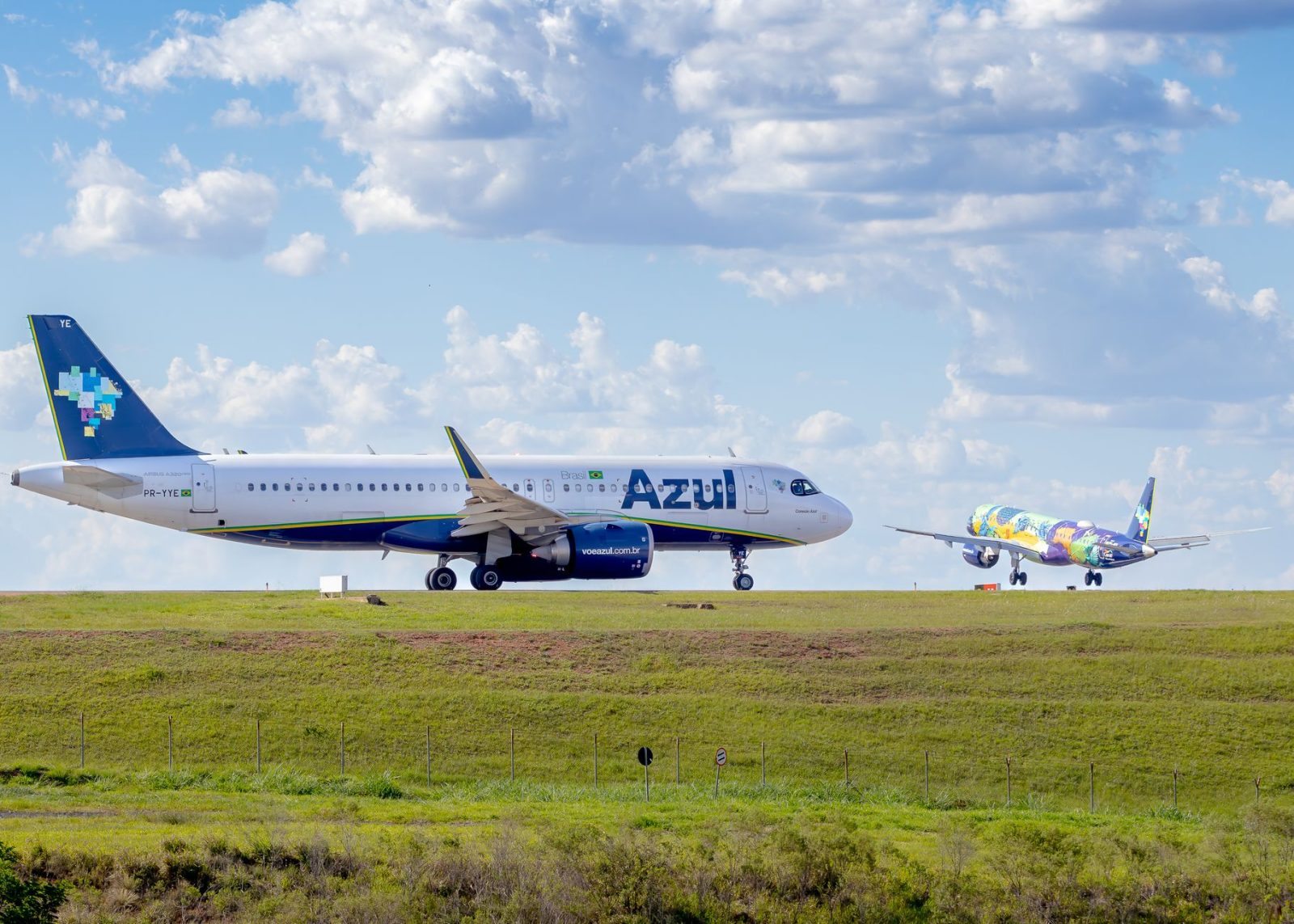 Aeronaves da Azul estacionadas ou em operação na pista de um aeroporto sob céu azul.