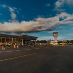 Pequeno terminal aeroportuário com pessoas caminhando pelo pátio sob céu azul
