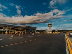 Pequeno terminal aeroportuário com pessoas caminhando pelo pátio sob céu azul