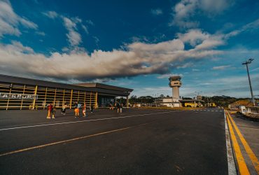 Pequeno terminal aeroportuário com pessoas caminhando pelo pátio sob céu azul