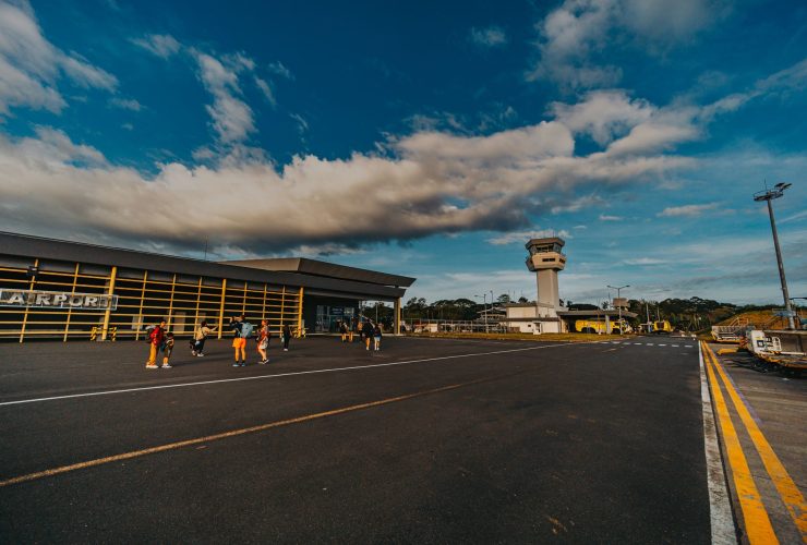 Pequeno terminal aeroportuário com pessoas caminhando pelo pátio sob céu azul