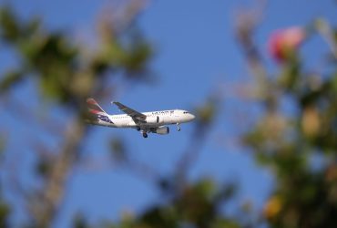 Avião comercial da LATAM voando sob céu azul sobre Florianópolis, no Brasil.