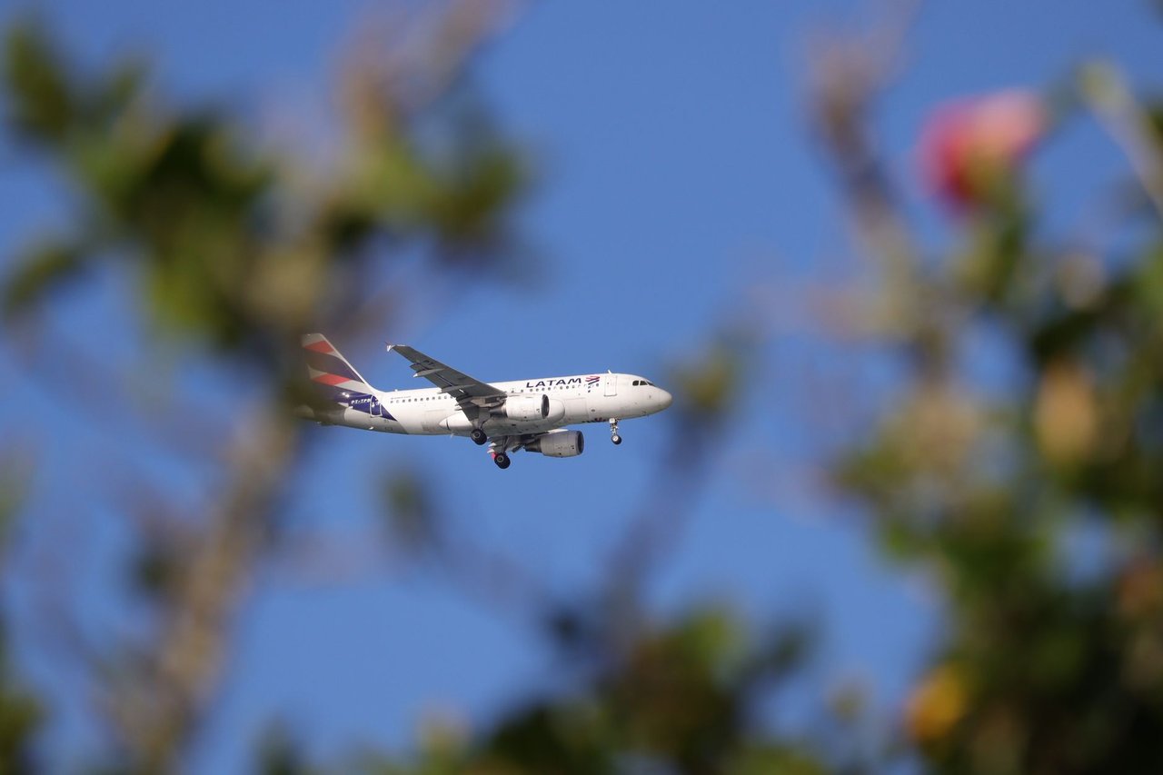 Avião comercial da LATAM voando sob céu azul sobre Florianópolis, no Brasil.