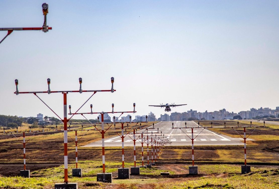 Avião pousa em uma pista de aeroporto, com a área urbana ao fundo