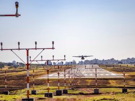 Avião pousa em uma pista de aeroporto, com a área urbana ao fundo