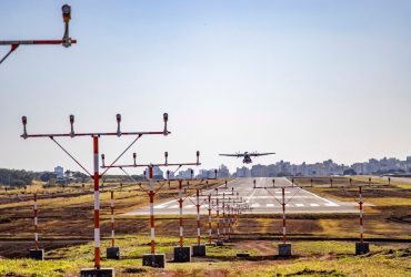 Avião pousa em uma pista de aeroporto, com a área urbana ao fundo