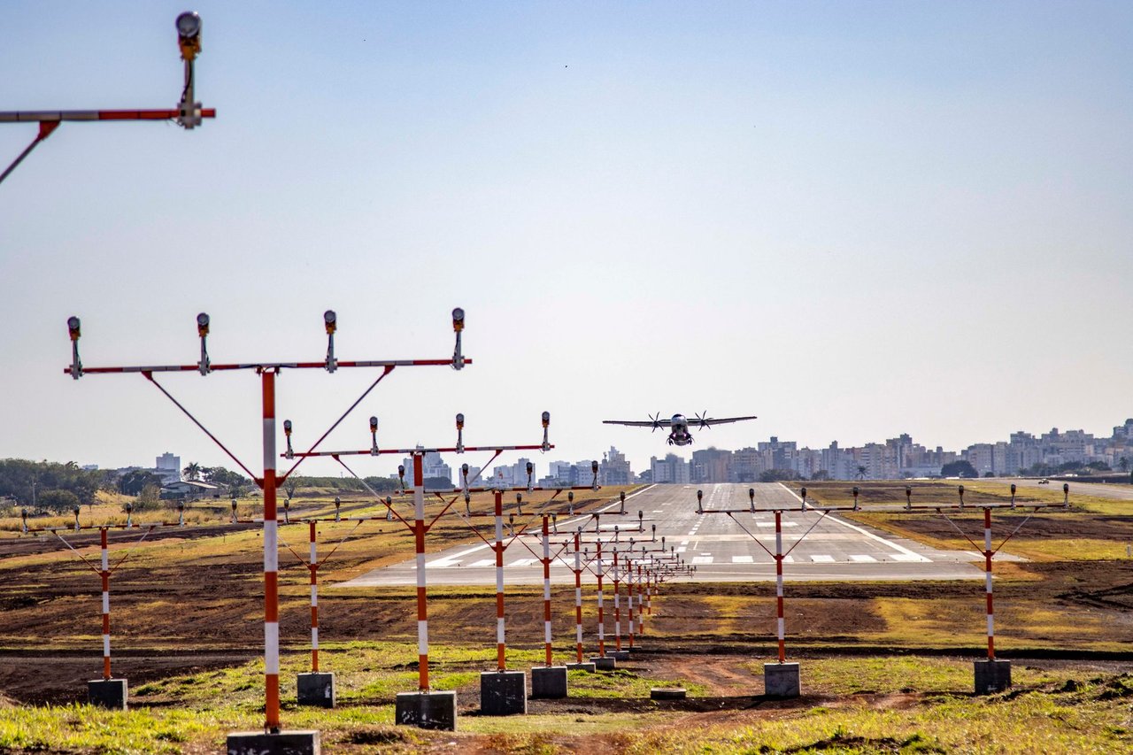 Avião pousa em uma pista de aeroporto, com a área urbana ao fundo