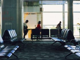 Terminal de aeroporto com fileiras de assentos e passageiros caminhando ao fundo.