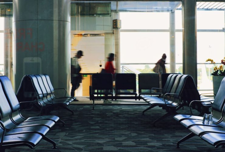Terminal de aeroporto com fileiras de assentos e passageiros caminhando ao fundo.