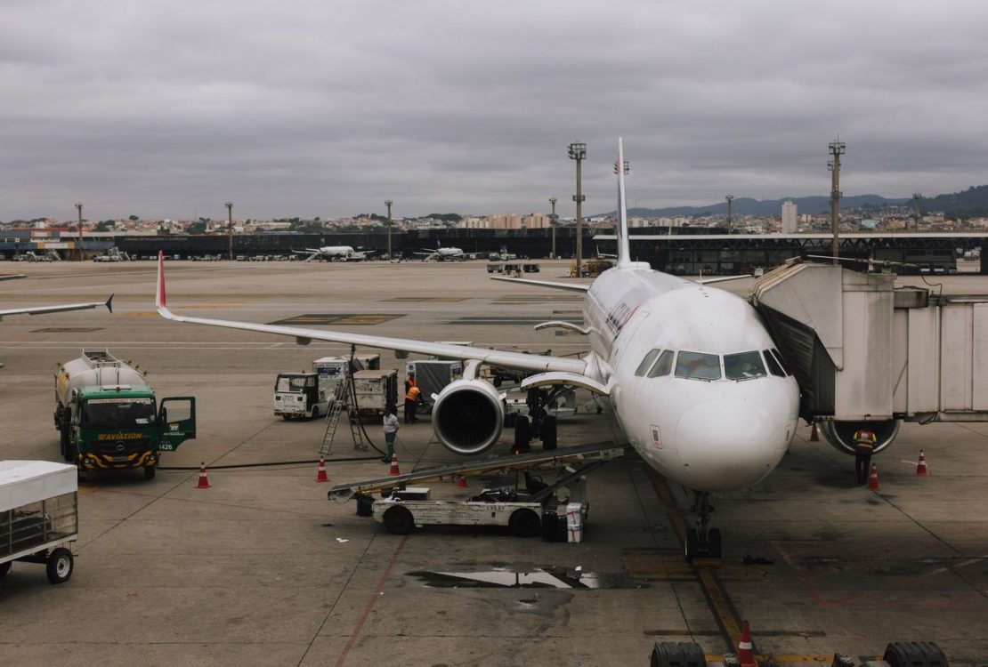 Avião sendo preparado em aeroporto de São Paulo junto a uma ponte de embarque e equipe de solo.