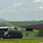 Caminhão de carga trafega por uma rodovia rural cercada por extensas áreas agrícolas.