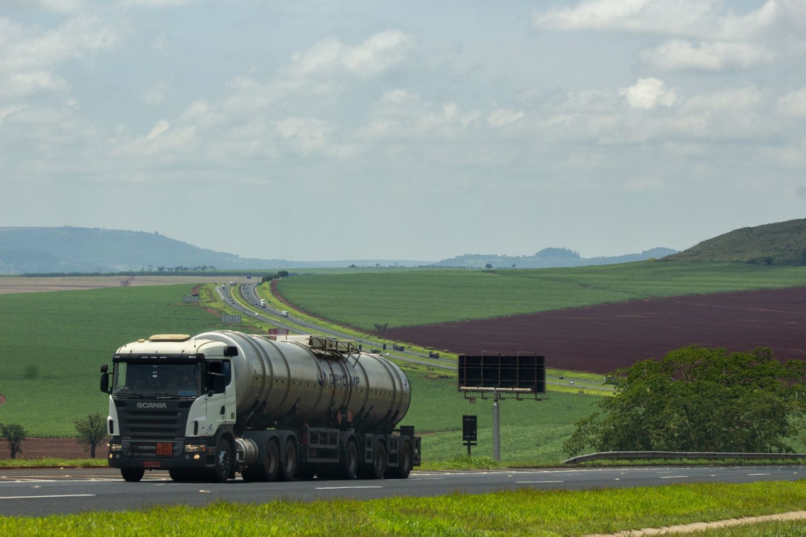 Caminhão de carga trafega por uma rodovia rural cercada por extensas áreas agrícolas.