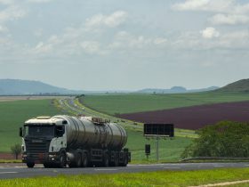 Caminhão de carga trafega por uma rodovia rural cercada por extensas áreas agrícolas.