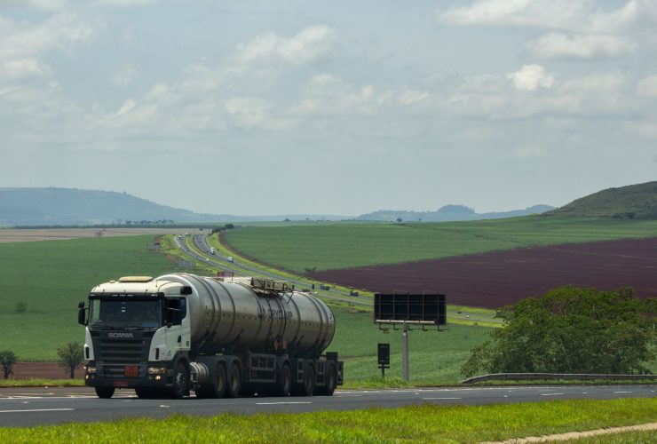Caminhão de carga trafega por uma rodovia rural cercada por extensas áreas agrícolas.