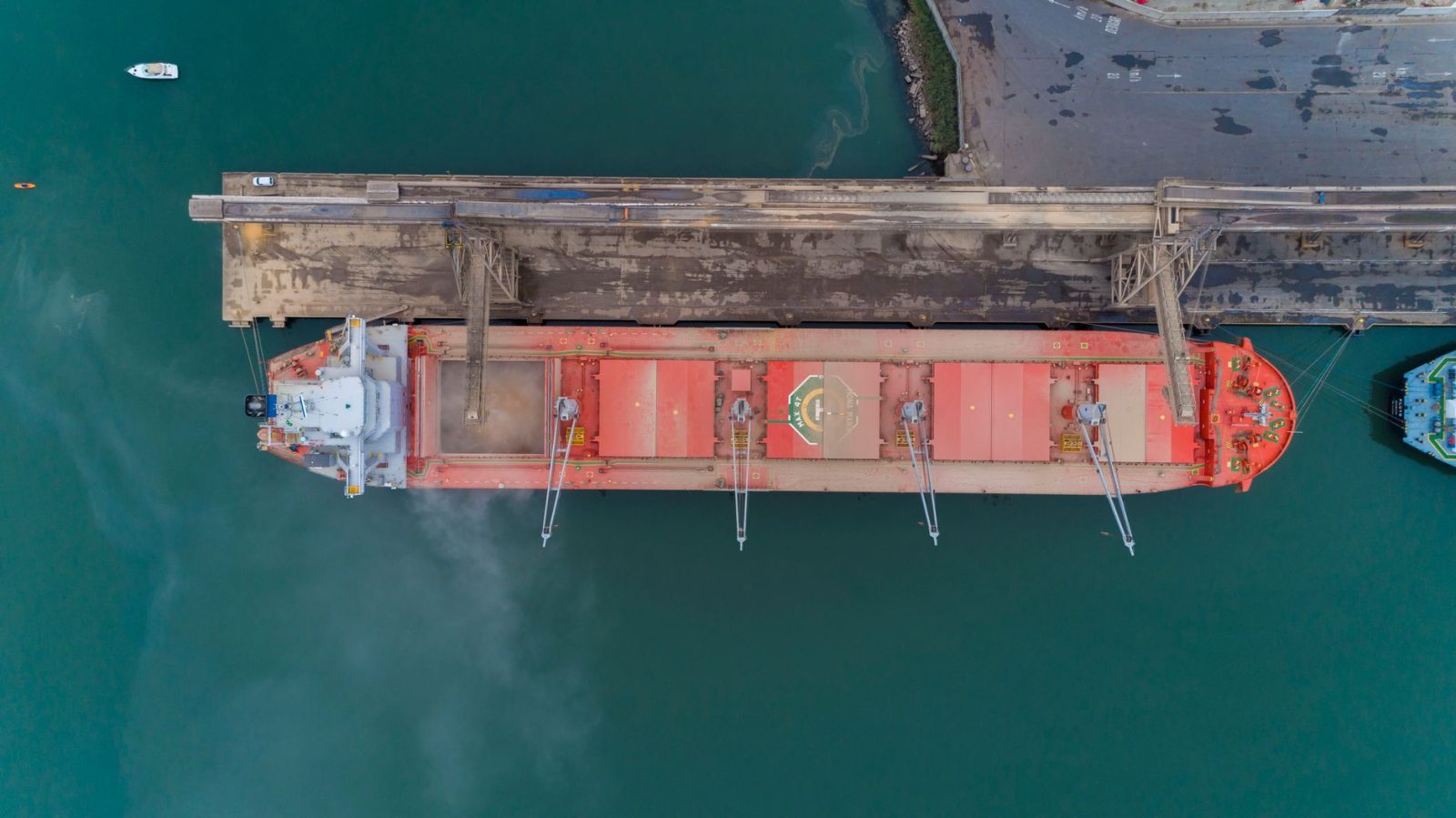 Vista aérea de um navio cargueiro atracado no porto de São Francisco do Sul, com instalações portuárias e movimentação marítima ao redor.