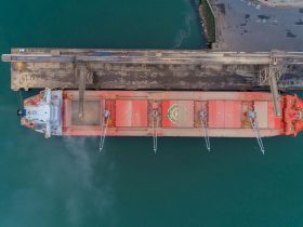 Vista aérea de um navio cargueiro atracado no porto de São Francisco do Sul, com instalações portuárias e movimentação marítima ao redor.