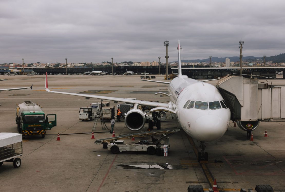 Aeronave comercial sendo preparada junto a uma ponte de embarque em um aeroporto de São Paulo, com equipe de solo no pátio.